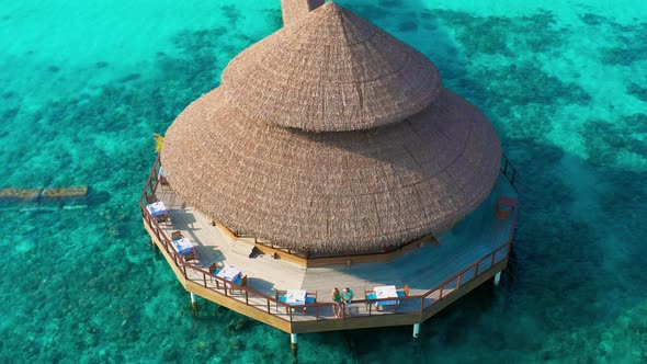 Aerial view on young couple in water restaurant with leaf roof on the beach in Maldives
