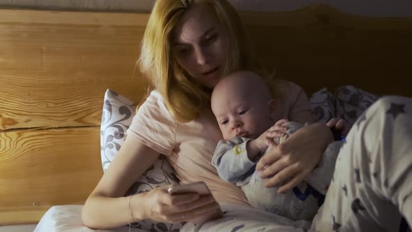 woman reads a fairy tale from a smartphone with a baby before bed in bed
