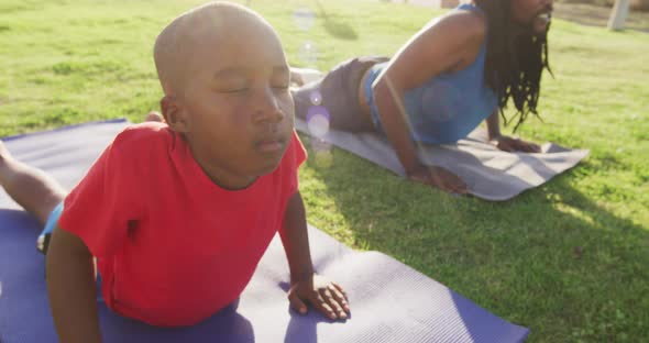 Video of african american son and father practicing yoga on grass on sunny day