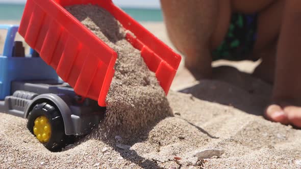 Baby Boy Playing on the Beach with Plastic Cars on a Sandy Beach Closeup