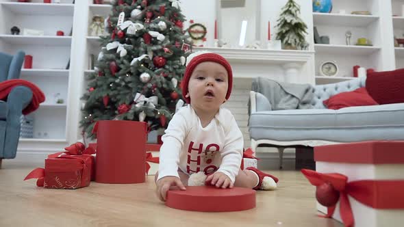 Little Baby Playing with Red lid of the Christmas Box Sitting on the Wooden Floor