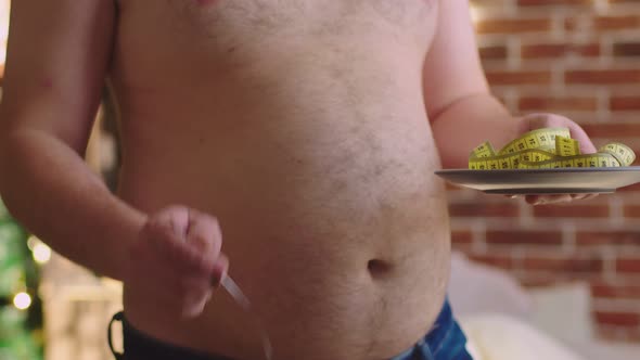 Obese Man Takes Plate with Measuring Tape and Winds It Fork Closeup His Stomach