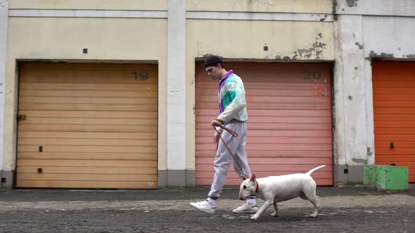 Portrait of Stylish Guy 20s in Sportswear Walking Along Street with His Pedigree Dog Holding