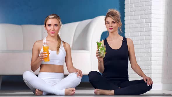 Two Fitness Woman Posing with Fresh Vitamin Cocktail Sitting Lotus Pose at Yoga Class Studio