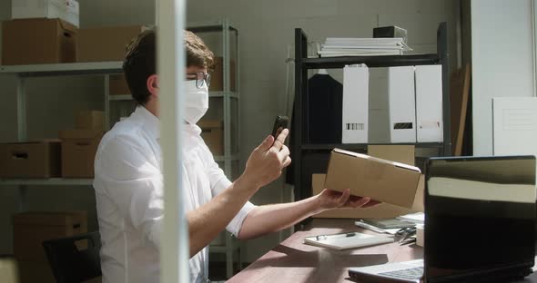 Man Employee of Warehouse Wearing Medical Mask Taking Delivery Box and Writing Information About