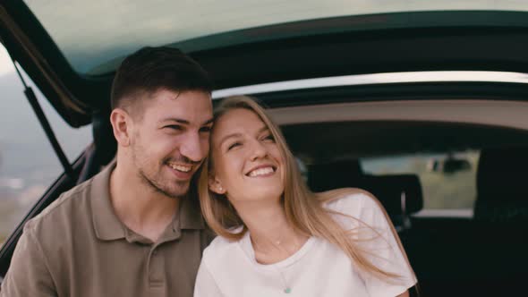 Young Traveler Couple on Road Trip in Mountains Sitting in a Trunk of a Car