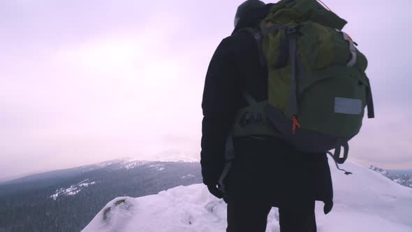 A Young Man, a Tourist, Stands on the Edge of a Snow-covered Mountain