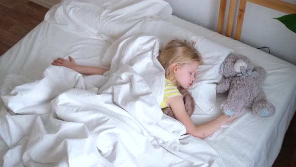 Blonde Little Girl Sleeping in Big Bed with White Bedding