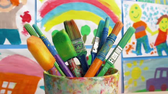 Paint Brushes In Classroom With Paintings On Wall