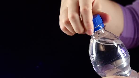 Hands Up and Opening a Blue Bottle of Fresh Water on Dark, Slow Motion, Splash, Spray, Bubbles