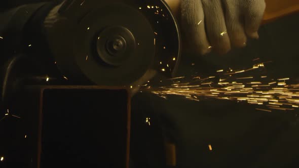 Industrial worker using an angle grinder and cutting a metal square pipe
