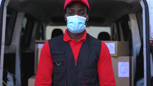 African delivery man carrying cardboard box while wearing face mask to avoid corona virus spread