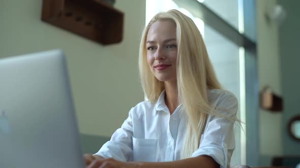 Closeup Face of Pretty Young Blonde Woman with Cute Smile Typing Something on Laptop Keyboard