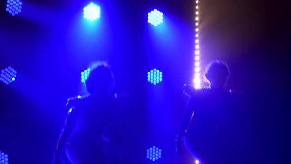 Silhouettes of Dancing Young Women on Stage in a Dark Studio with Smoke and Neon Lighting. Bright