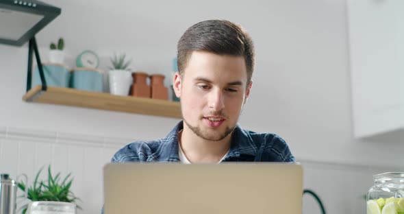 Man Talks Online Using Video Call on Laptop in Kitchen, Drinks Coffee in Morning