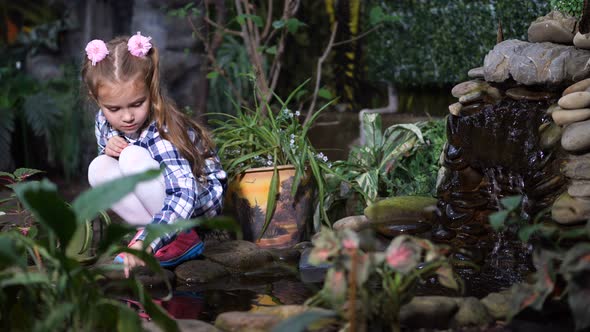 A Girl Sits Near a Streamlet and Runs Her Finger Along the Water