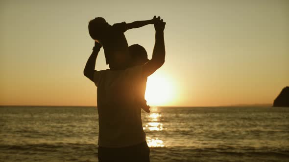 Father and Son Silhouettes Playing on Beach, Boy Raising Up Hands Imitating a Flight at Wonderful
