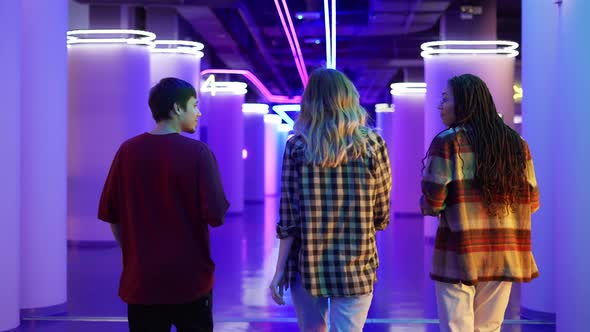 Group of Three Friends Walking By Cinema Hall with Neon Interior Rear View