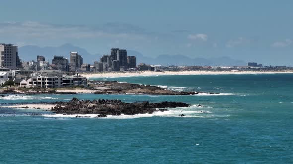 Rocky shore and buildings in Small Bay beach, Cape Town, South Africa, with Bloubergstrand in backgr