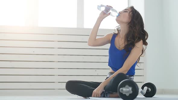 Young Woman Is Drinking Water After Training on the White Interior