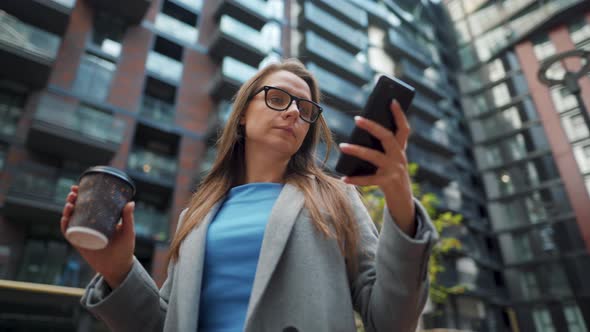 Formally Dressed Woman Standing in a Business District with Thermo Cup in Hand and Using a