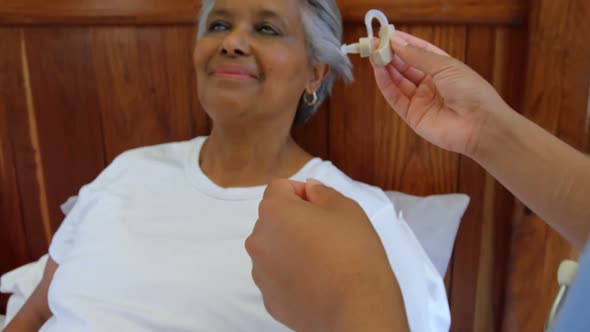 Female doctor inserting hearing aid in senior black woman ear in a comfortable home 4k