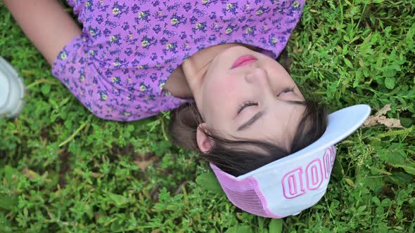 A cute teenage girl in a cap and a pink T-shirt lies on the grass and smiles