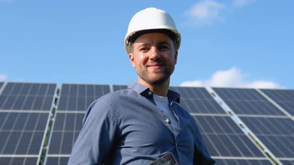 Happy Caucasian Engineer in Helmet Smiling at Camera at Solar Power Station Outside