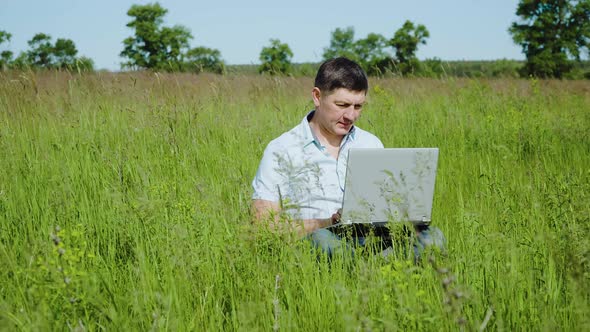 Businessman Works Behind a Laptop Sitting on the Grass