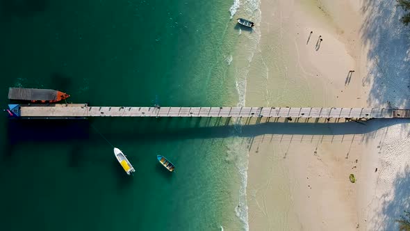 Aerial top down view of white sand beach with long tail boat docked at the pier on 4k Beach, Koh Ron
