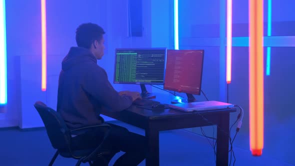 Young African Man Writing Hacker Programs in Dark Room with Neon Lights