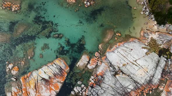 Aerial of Bay of Fires bright orange rocks with waves in rock pools in the sea. Binalong Bay, Tasman