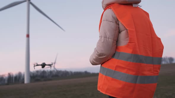 Female Engineer Uses a Drone to Check a System Performance of Wild Turbine or Windmill at Sunset