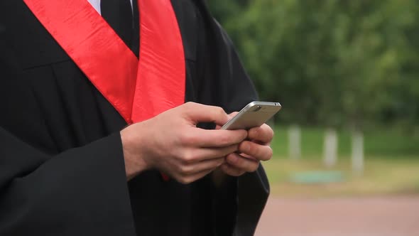University Graduate Browsing News on Smartphone, Male in Gown Sliding Pages