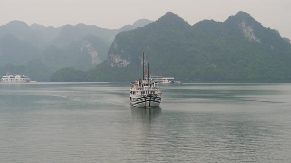 Ship cruising in Halong Bay while other boats are anchored with misty horizon