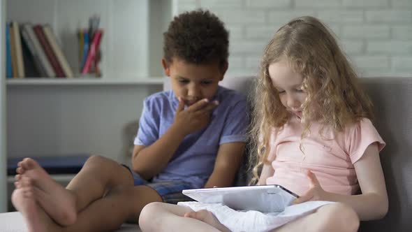 Two Multiracial Children Sitting on Cozy Sofa and Watching Cartoons on Tablet