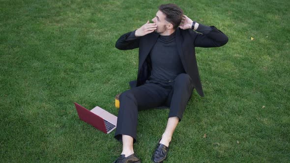 Confident Man in Elegant Suit Sitting on Green Spring Summer Lawn with Laptop Surfing Internet