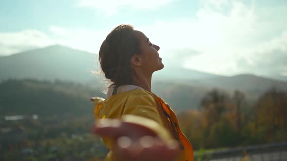 Young Woman Wearing a Yellow Jacket Raising Her Arms Into the Blue Sky and Enjoying the View Above