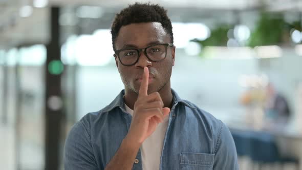 Portrait Shot of Young African Man Showing Quiet Sign Finger on Lips
