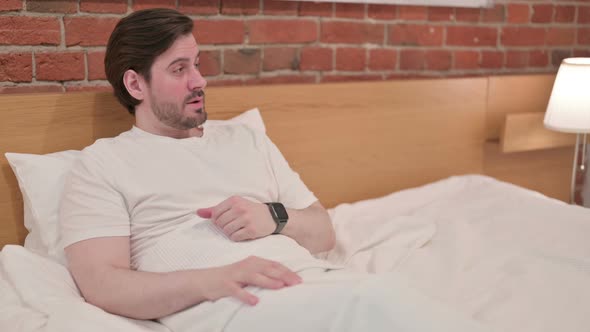 Casual Young Man Checking Watch While Waiting in Bed