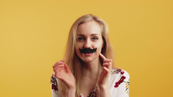 Studio Shot of Funny Humorous Blonde Caucasian Woman with Black Fake Mustache Under Her Nose Over