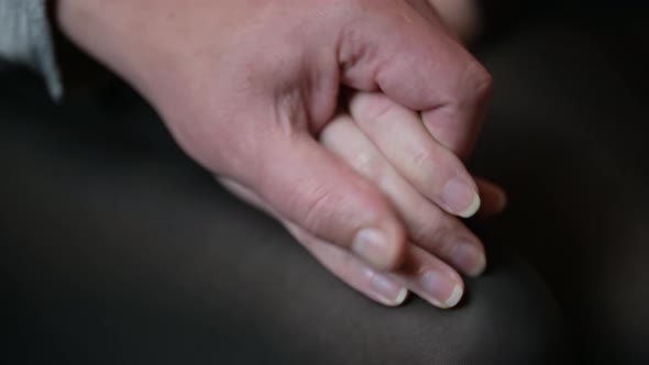 Close-up of a man takes a woman's hand. The couple is sitting on the couch.