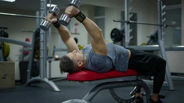 Strong Masculine Sportsman Lying on Exercise Bench Lifting Dumbbells