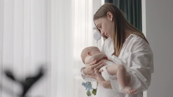 Mother Standing Near Window and Holding Her Baby Son