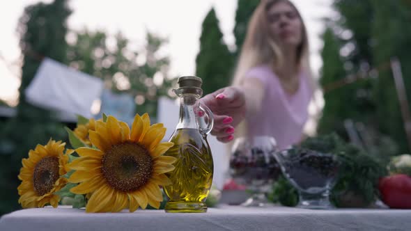 Female Hand Taking Glass Decanter with Sunflower Oil in Slow Motion Cooking Salad Outdoors