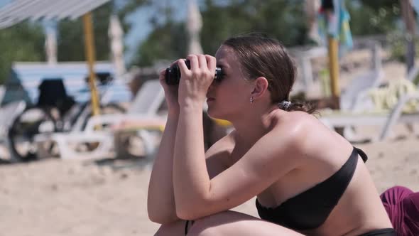 Beautiful Girl Looks Through Binoculars on the Beach