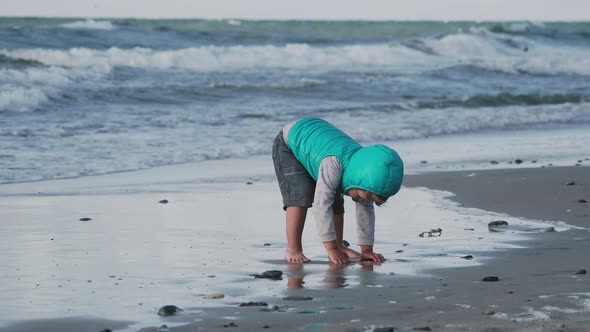 Toddler Boy in Waistcoat Is Playing with Sand on Sea Side.