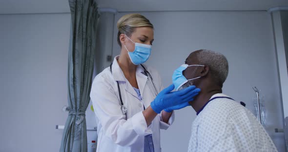 Caucasian female doctor wearing face mask examining throat of african american senior male patient