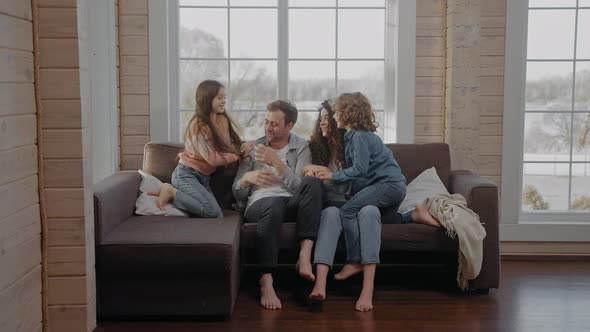 Young Family Sit Together on a Couch Tickling and Smiling Looking at Camera