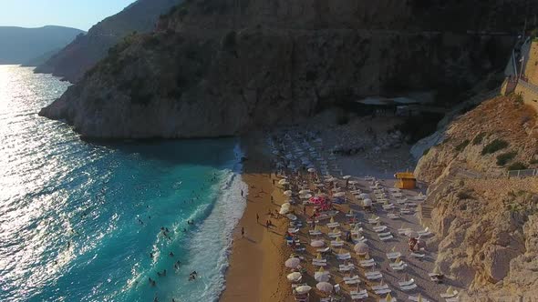 People Swim on Light Blue Sea in the White Sandy Beach Near the Rocky Mountainside